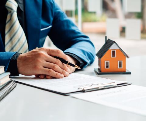 A person sorting their tax affairs at a desk with files, pen and a small model house