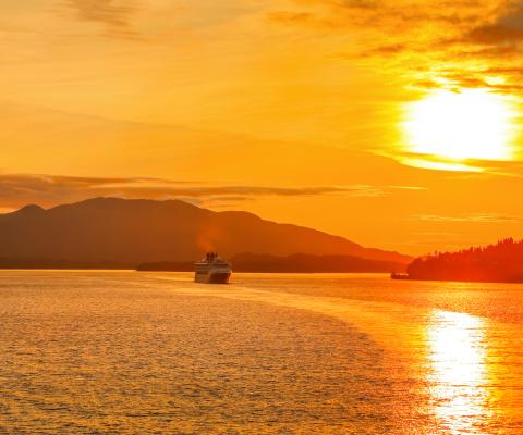 The sun sets over a cruise ship casting yellow light over the water