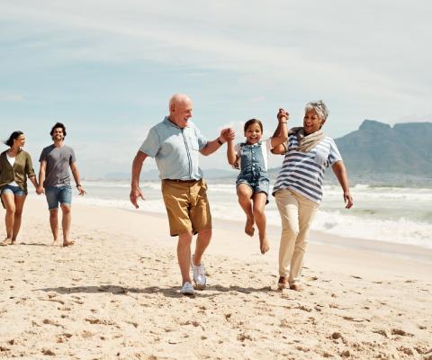 Grandparents play with their grand-daughter on the beach while parents walk behind
