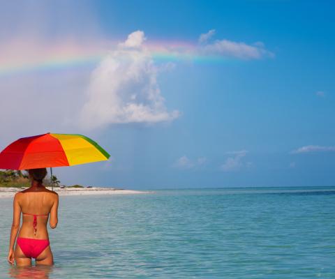 A woman pictured in the sea with an umbrella beneath a rainbow