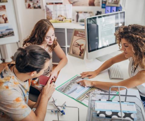 A travel agent helps a young couple with an enquiry