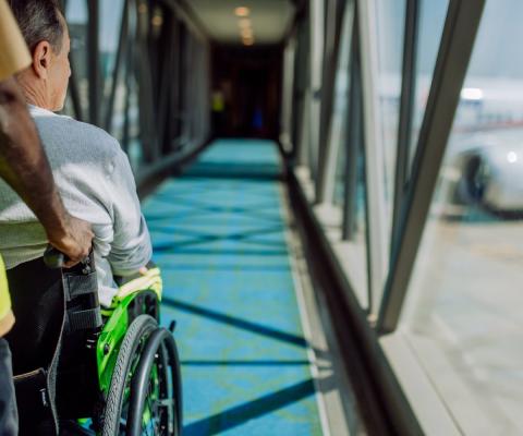 A air traveller being pushed down an air bridge onto an aircraft in a wheelchair