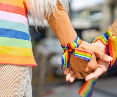 Two people wearing rainbow wristbands clasp hands