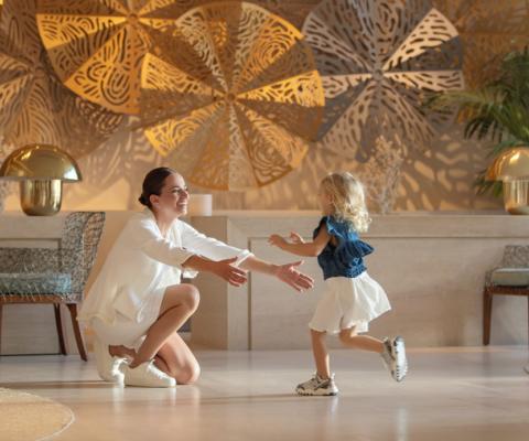Girl toddler running into the arms of her smiling mum in hotel lobby