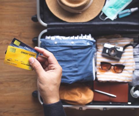 A person holding two bank cards with a half-packed suitcase in the background