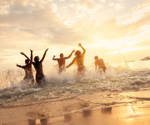 Friends splashing on beach, silhouetted by sunset
