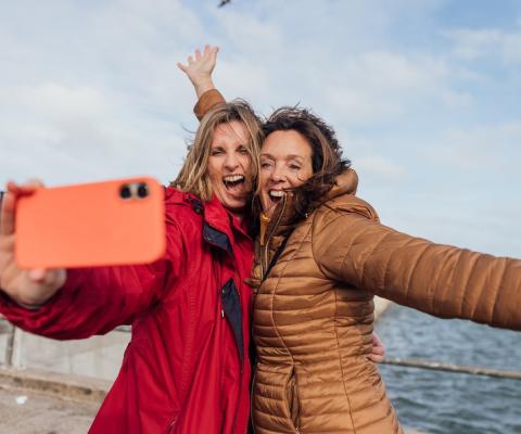 Two women take a selfie with the sea in the background