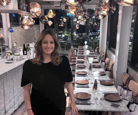 Sara Greene, brown-haired smiling woman standing in front of long dining table 