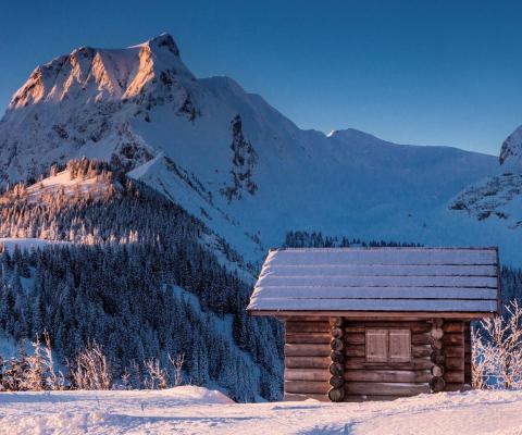 A small wooden snow-dusted house with mountain rising in background