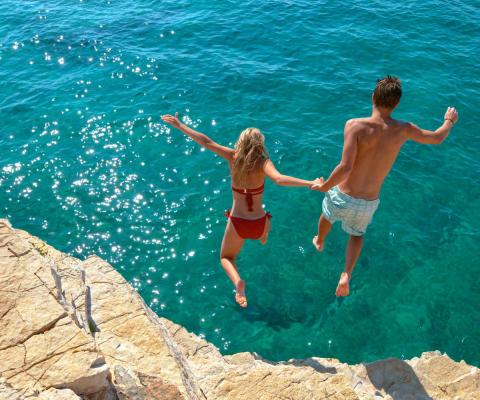 Couple jumping from small cliff into sea
