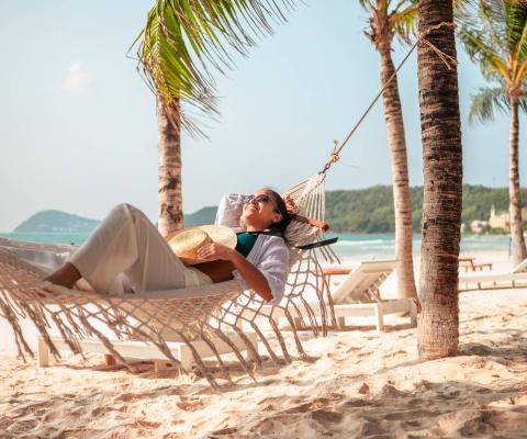 A woman relaxes on a hammock in a tropical beach location with palm trees