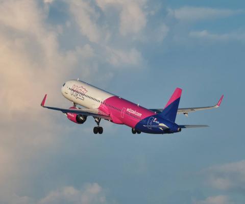 Wizz Air plane mid-flight against a slightly cloudy backdrop
