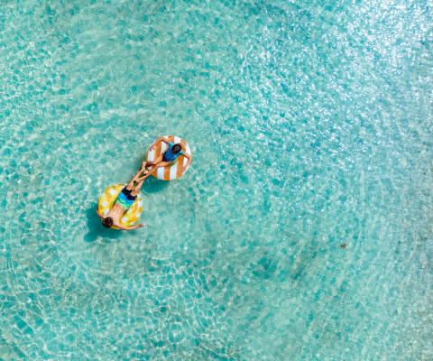 Birds-eye view of two people floating in clear sea on inflatable rubber rings