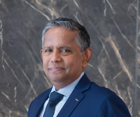 Grey-haired man with light brown skin smiling in blue suit