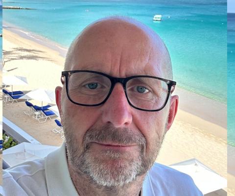 Up-close portrait of white middle-aged man with black rimmed glasses and beard, sunny beach background 