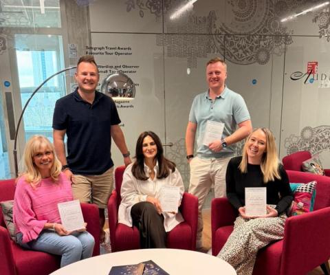 A work team with two men standing, three women sitting, all smiling 