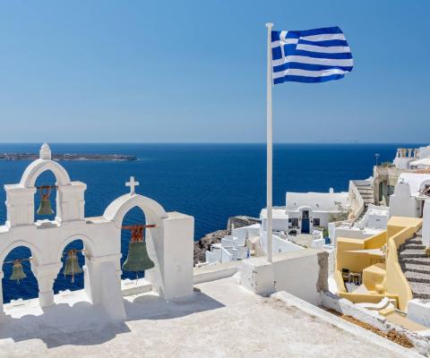 Greek orthodox church with bells and greek flag against famous white houses on Santorini island, Aegean sea, Greece