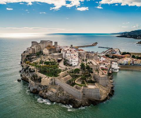 A medieval stone fortress built on a high rocky peninsula, overlooking the blue Mediterranean Sea under a clear sky