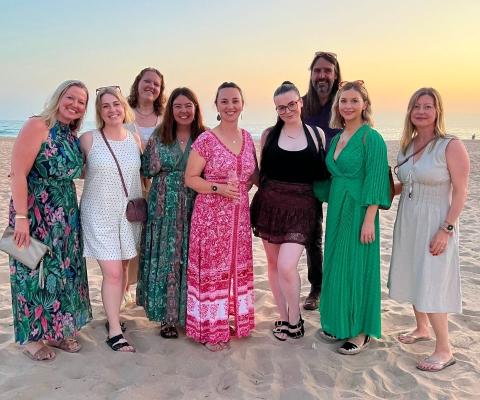 People standing on a white sand beach with the sunset behind them