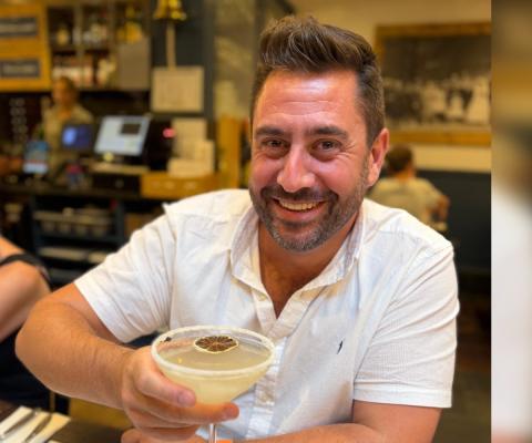 White man with brown short hair smiling and holding cocktail 