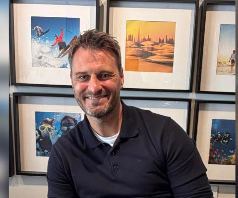 White man smiling with framed travel-themed pictures behind him  