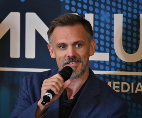 White man speaking on stage with microphone
