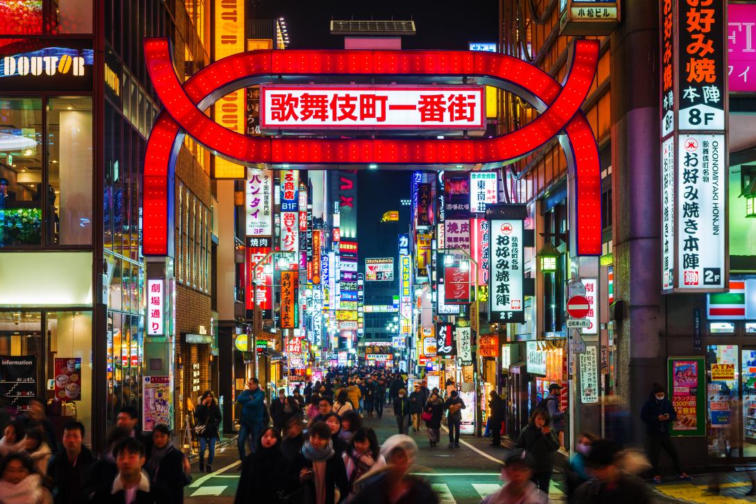 Neon lights and illuminated billboards of Shinjuku glittering at night above crowds of shoppers in the heart of Tokyo