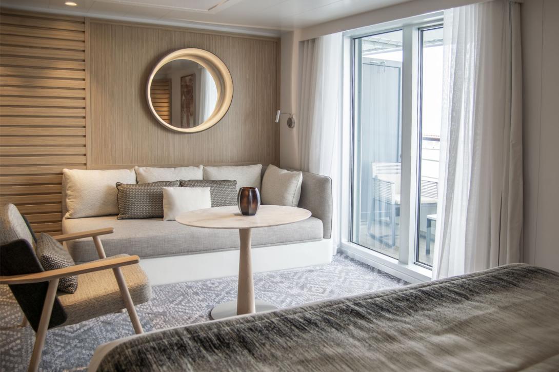 Luxury cabin suite on ship, image of grey sofa with mirror on wall and French windows opening onto balcony