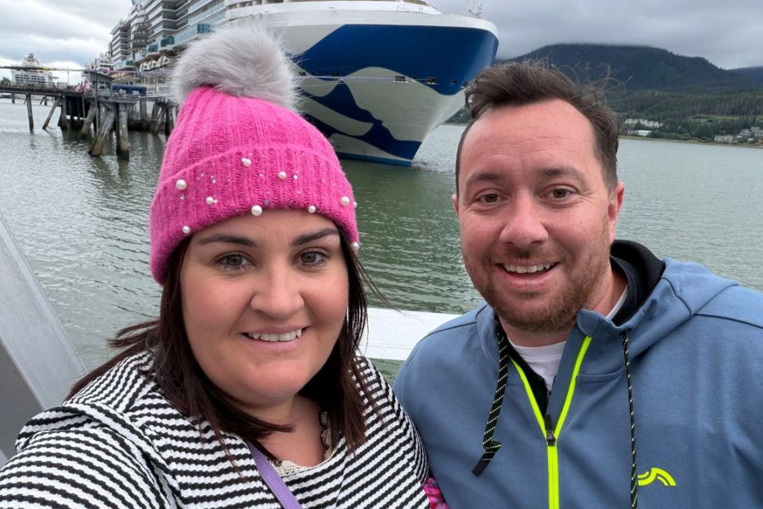 Man and woman smiling in front of cruise ship
