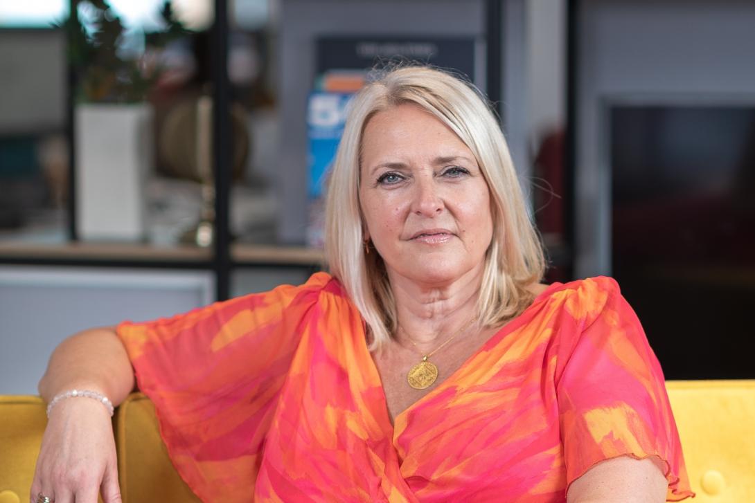 Professional headshot of woman with blonde hair and coral dress