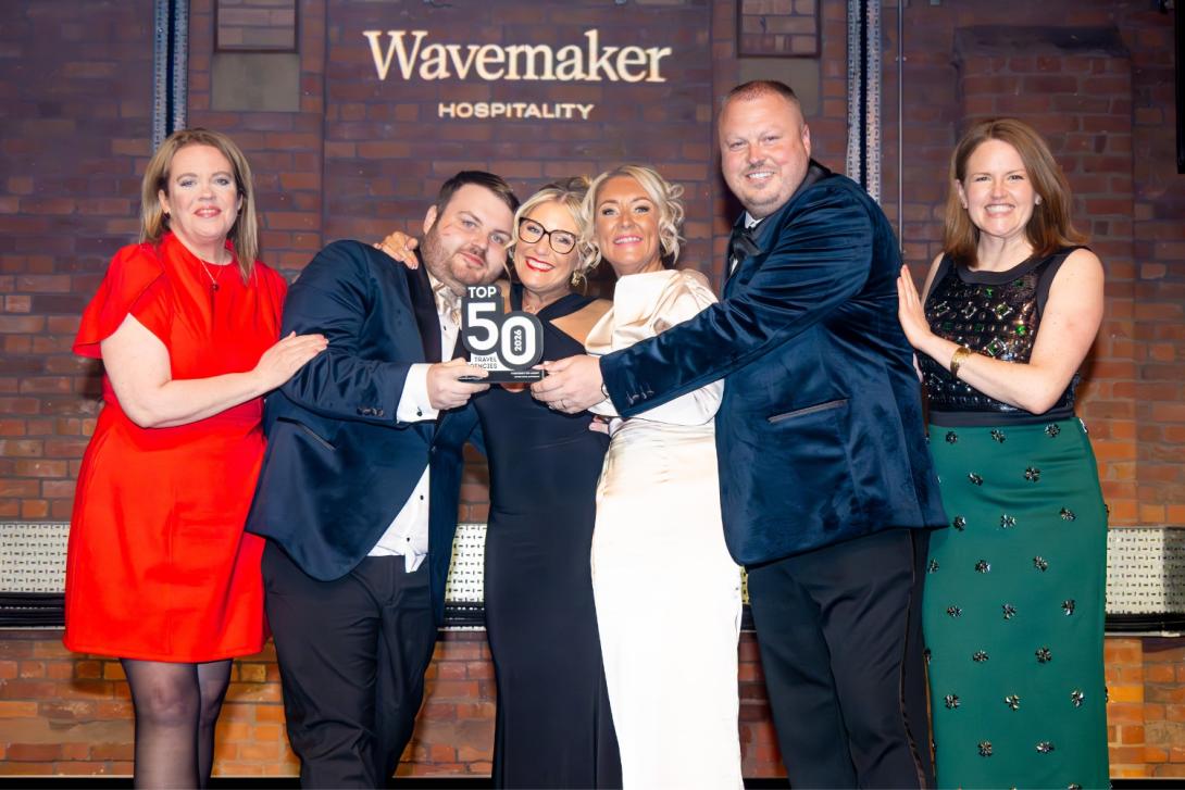 Group of six people at a travel awards show, four women and two man. Man on the second left holding trophy