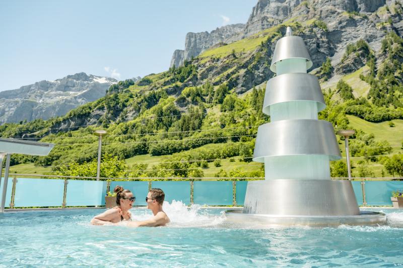 A couple in a swimming pool with mountain and greenery in the background