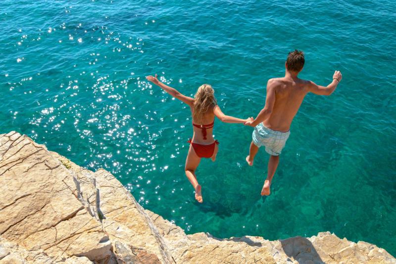 Couple jumping from small cliff into sea