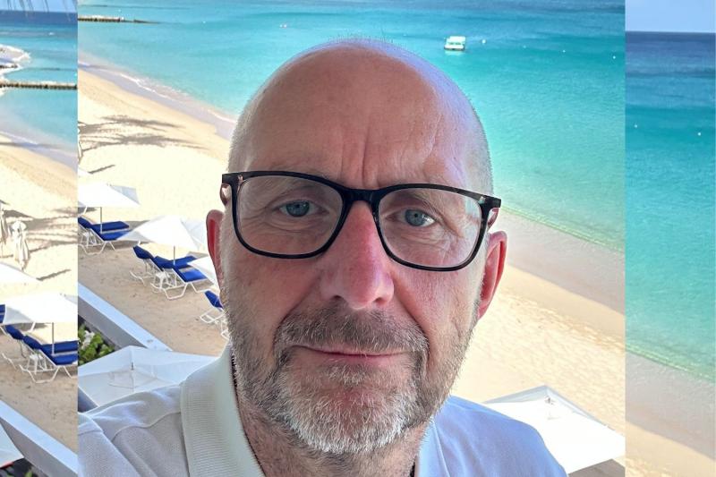 Up-close portrait of white middle-aged man with black rimmed glasses and beard, sunny beach background 