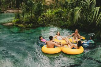 People in rubber rings floating on clear blue hot spring water with trees around